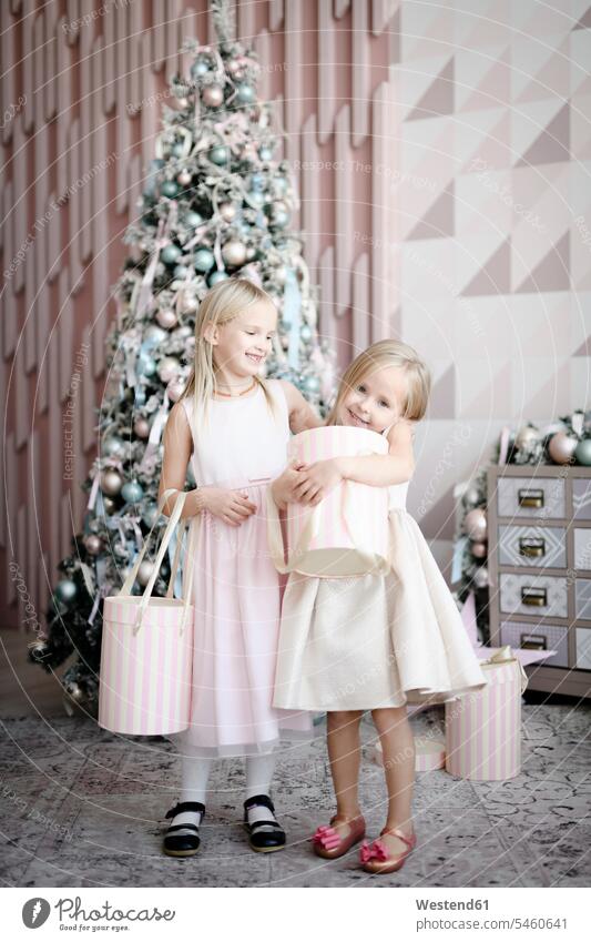 Portrait of two happy little girls standing in front of lighted Christmas tree with gift boxes human human being human beings humans person persons