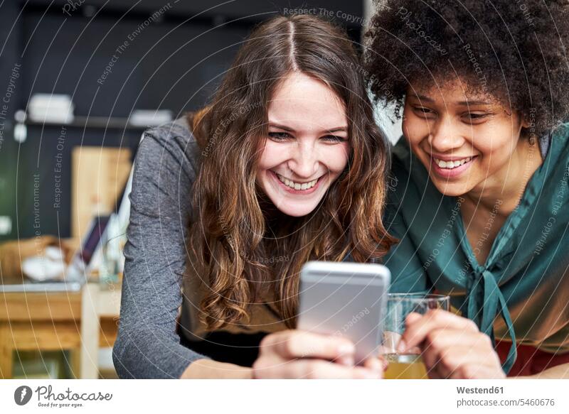 Two smiling young women sharing cell phone in office mobile phone mobiles mobile phones Cellphone cell phones share smile woman females offices office room