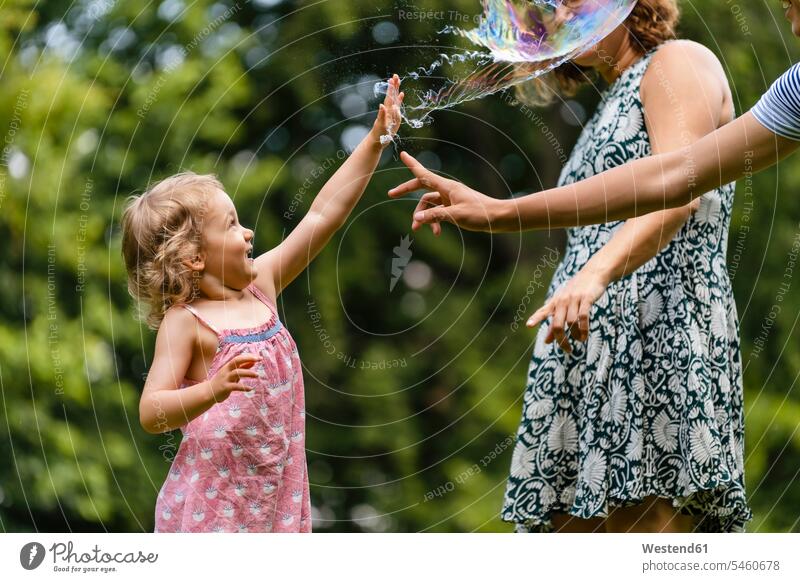 Girl exploding bubble while playing with family at park color image colour image outdoors location shots outdoor shot outdoor shots day daylight shot