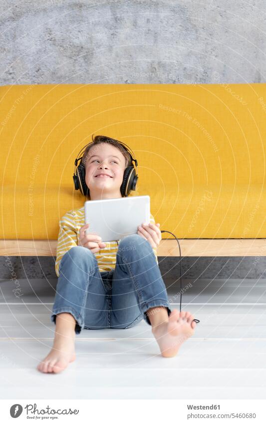 Boy playing with tablet and wearing headphones at a yellow couch jumper sweater Sweaters couches settee settees sofa sofas headset hear learn smile Seated sit