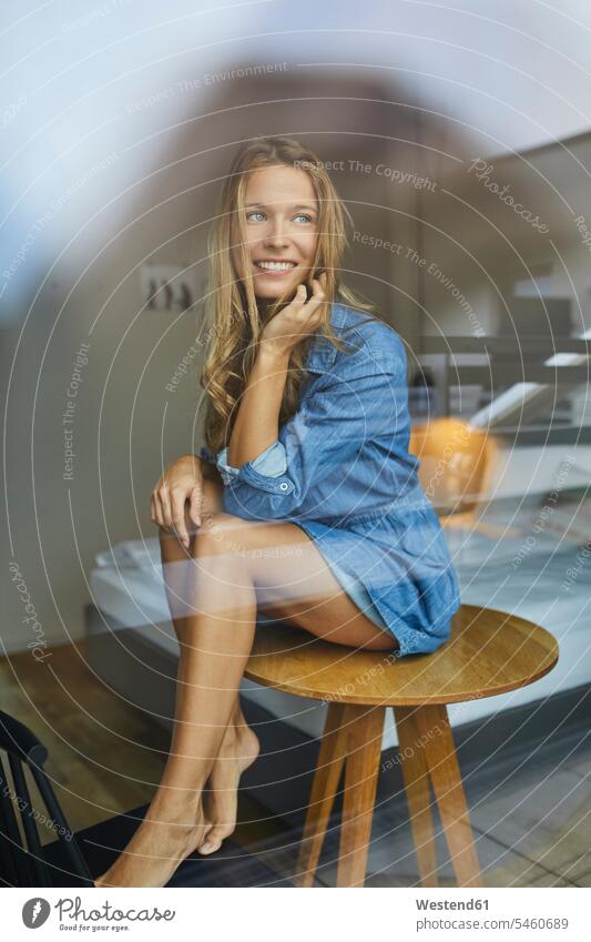 Smiling young woman sitting on table behind windowpane window glass window glasses windowpanes Window Pane Seated females women Table Tables smiling smile