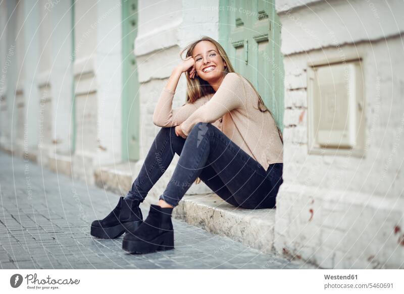 Laughing young woman sitting on step in front of an entrance door steps stair entry door entrance doors females women laughing Laughter Adults grown-ups