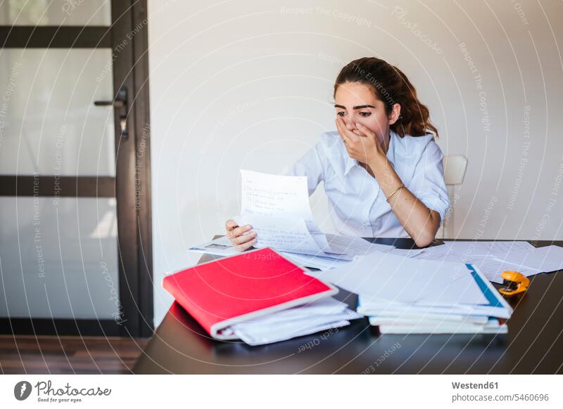 Shocked female student reading document at desk at home Tables desks learn Seated sit study pessimistic surprising surprised despaired Desperation Emotions