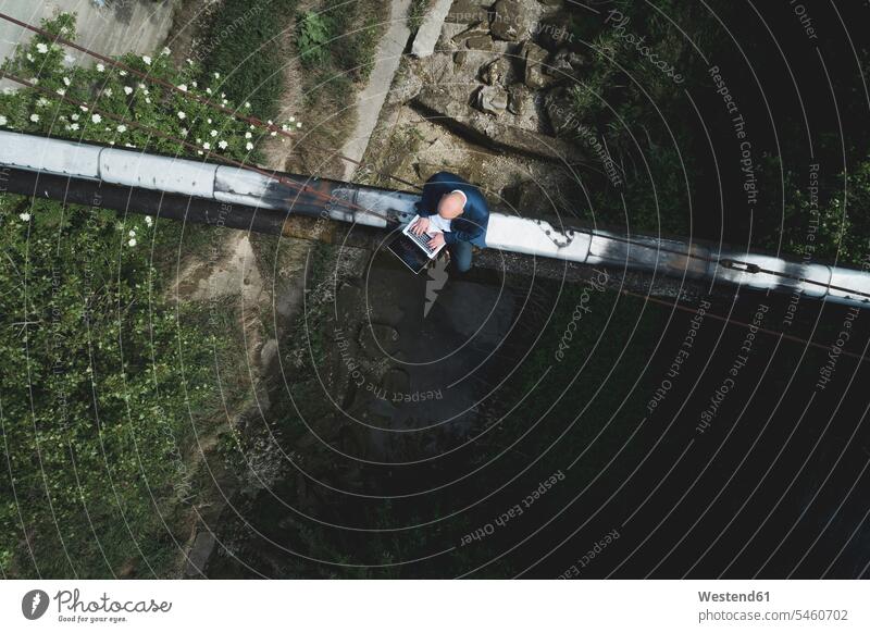 Aerial view of bald businessman using laptop while sitting on old pipes color image colour image Austria outdoors location shots outdoor shot outdoor shots day