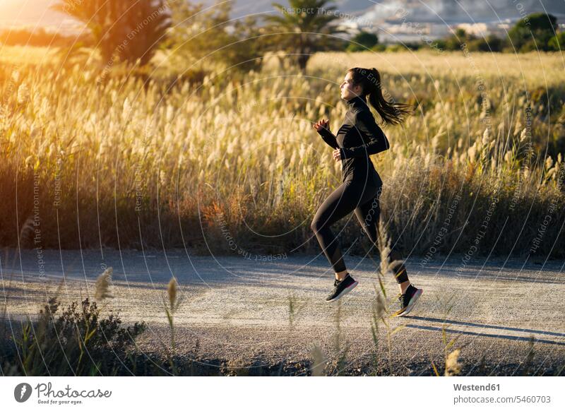 Young woman running on footpath against green landscape at sunset color image colour image Spain Sportswear Sports Wear Sport Clothes Activewear Sports Clothing