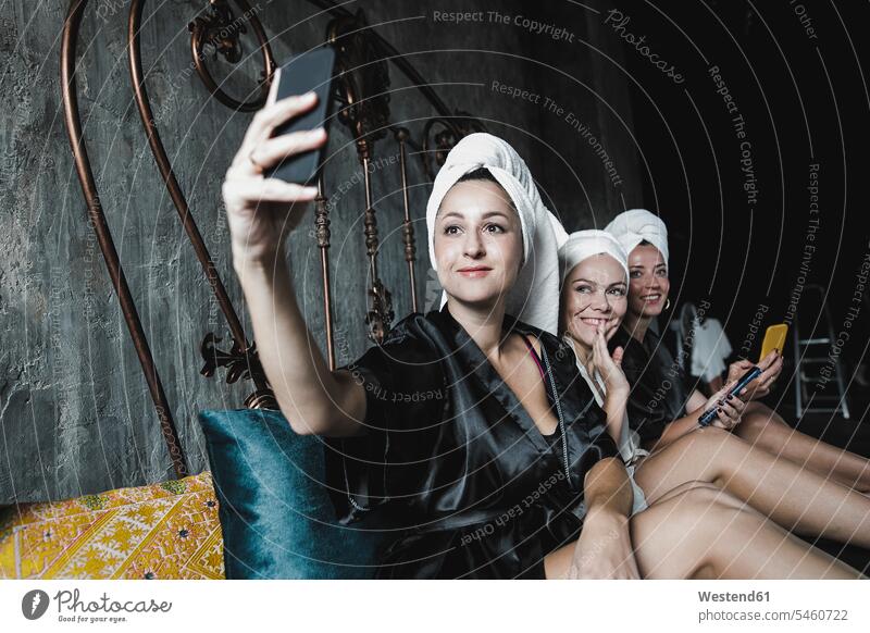 Three women with towels around her heads on bed taking a selfie female friends woman females Selfie Selfies beds mate friendship Adults grown-ups grownups adult