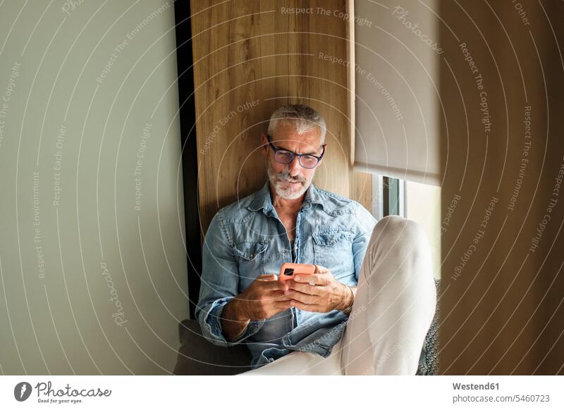 Smiling mature man using mobile phone in living room at home color image colour image indoors indoor shot indoor shots interior interior view Interiors morning