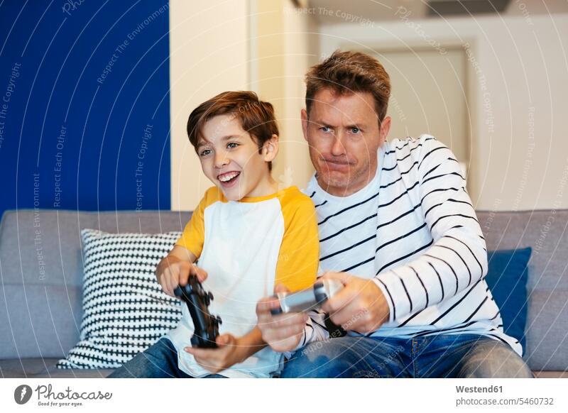 Father and son playing video game on couch at home sons manchild manchildren settee sofa sofas couches settees video games father pa fathers daddy dads papa