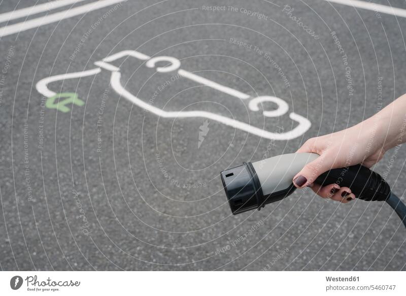 Germany, Hand of woman holding plug of electric vehicle charging station outdoors location shots outdoor shot outdoor shots day daylight shot daylight shots