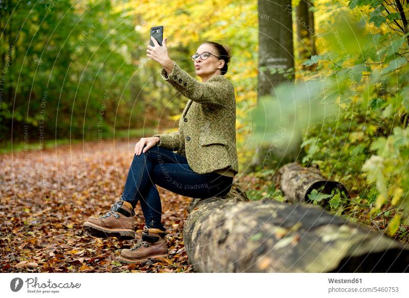 Mature woman taking a selfie in a autumn forest coat coats jackets telecommunication phones telephone telephones cell phone cell phones Cellphone mobile