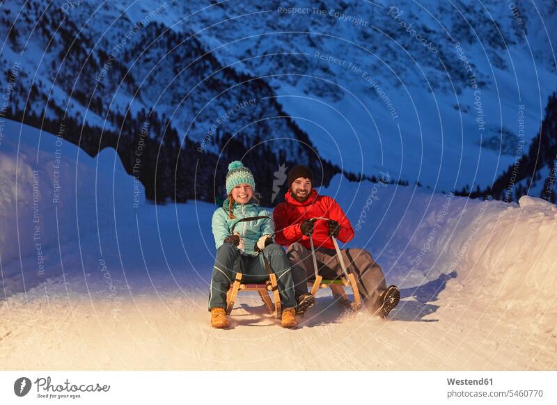 Happy couple sledding in snow-covered landscape at night snow covered covered in snow snowy by night nite night photography tobogganing landscapes scenery