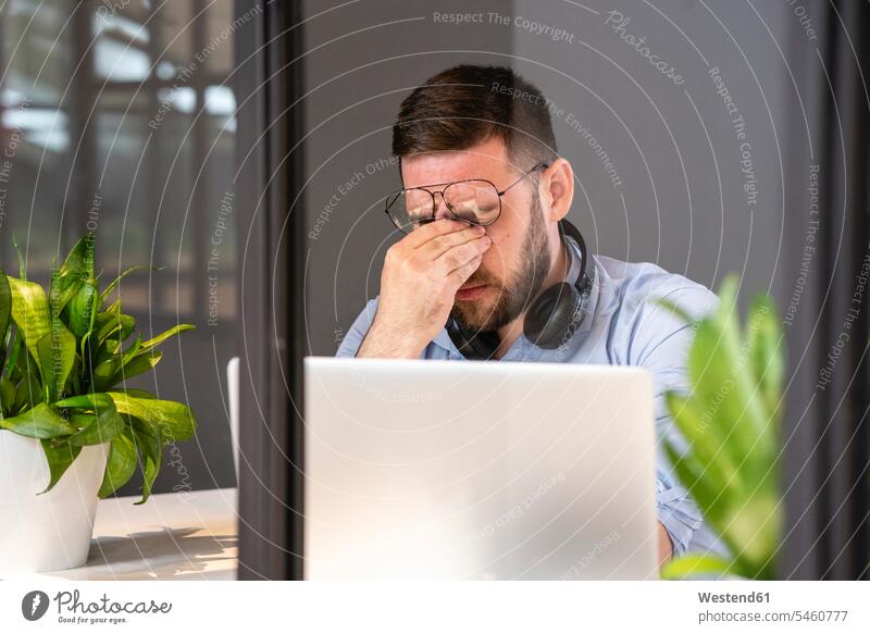 Tired handsome male professional with laptop seen through glass wall in creative coworking office color image colour image Businessman Businessmen Business man