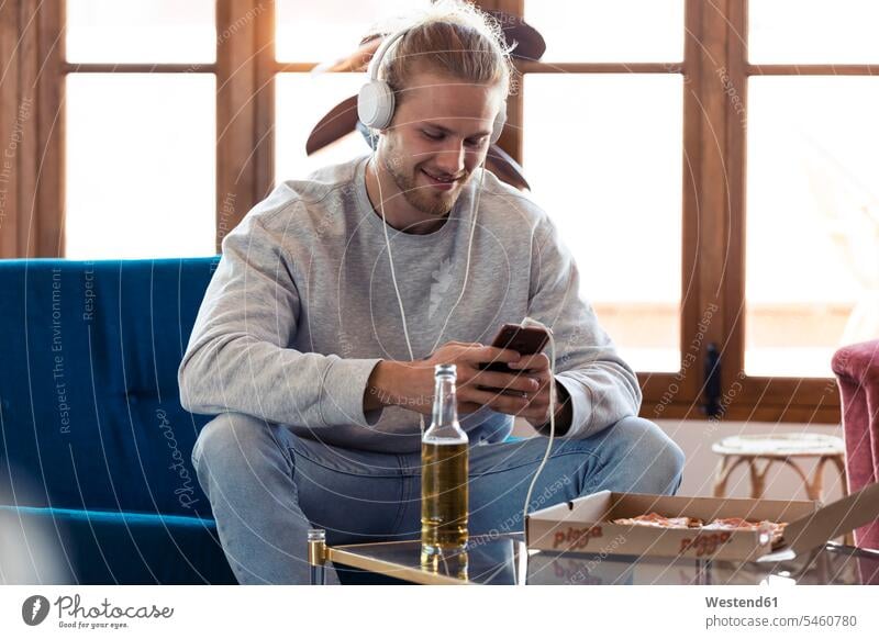 Smiling young man sitting on couch with cell phone and headphones human human being human beings humans person persons celibate celibates singles