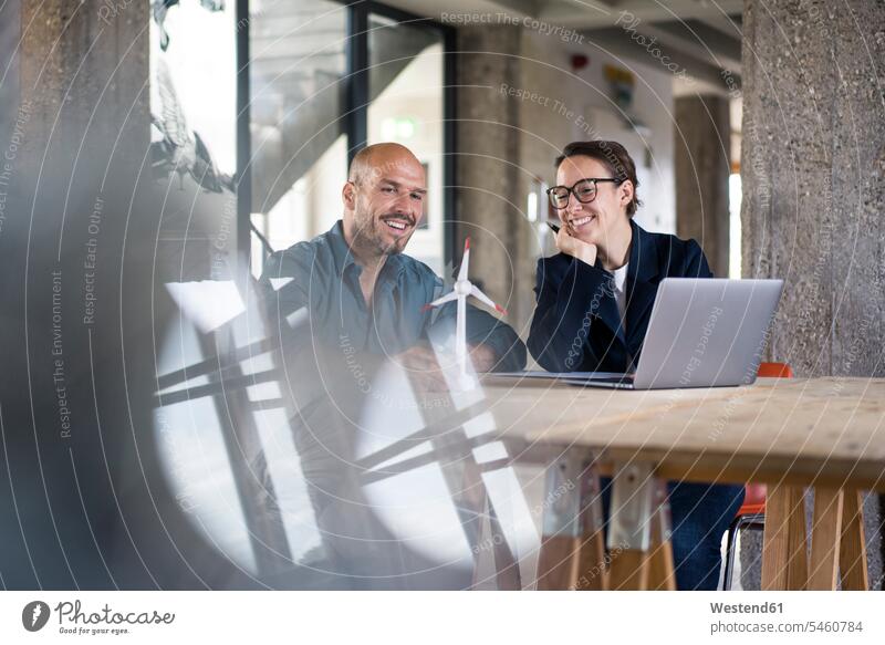 Business people with laptop looking at wind turbine toy while sitting at office color image colour image indoors indoor shot indoor shots interior interior view