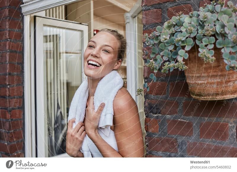 Happy sporty young woman with towel around her neck at house entrance sportive sporting athletic towels happiness happy females women sports Adults grown-ups