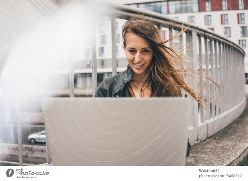 Portrait of smiling young woman with windswept hair using laptop on motorway bridge freeway motorways freeways Laptop Computers laptops notebook females women
