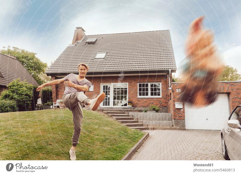 Mature man kicking away garden gnome in front of his home house houses garden gnomes men males building buildings built structure built structures