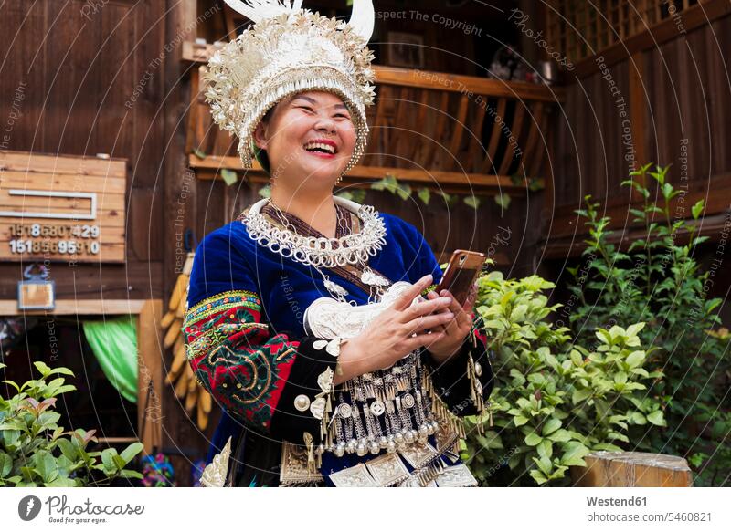 China, Guizhou, laughing Miao woman wearing traditional dress and headdress holding cell phone Smartphone iPhone Smartphones festive headgear headgears