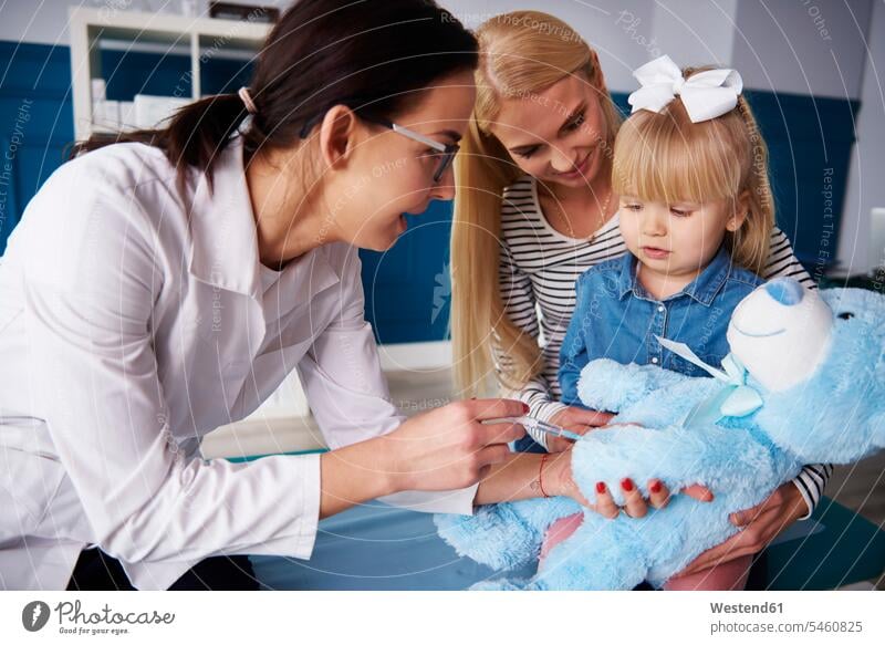 Doctor and girl with mother vaccinating teddy in medical practice inoculating vaccinate inoculate Female Doctor physicians Female Doctors examining checking