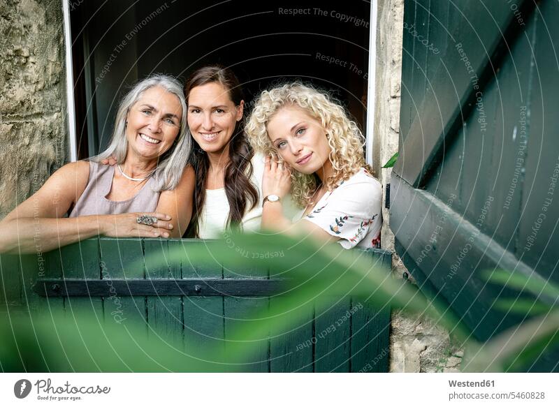 Portrait of three smiling women of different age behind stable gate age difference difference in age woman females portrait portraits gates smile animal stall