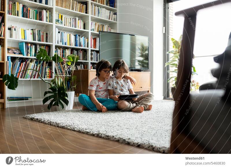 Two brothers sitting on floor in the living room with digital tablet human human being human beings humans person persons caucasian appearance