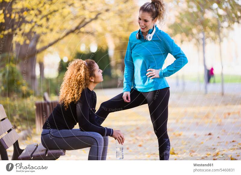 Two sportive young women talking in park woman females sporting sporty athletic parks speaking female friends Adults grown-ups grownups adult people persons