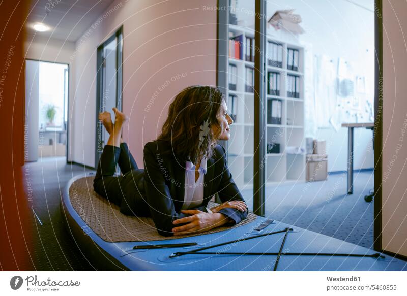 Businesswoman lying on paddle board, daydreaming in office Paddleboard standup paddleboard Paddleboards offices office room office rooms barefoot naked feet