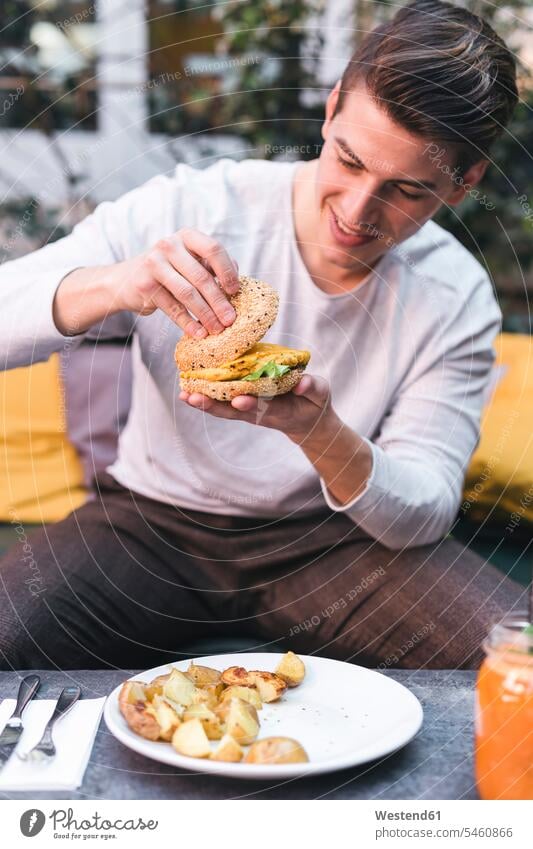Young man sitting on couch in a restaurant having a vegan burger for lunch model models casual leisure wear casual clothing casual wear casual clothes