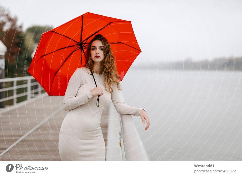 Portrait of young woman with red umbrella, leaning on railing during rainy day dresses Brolly umbrellas hold aspirations Crave Craving longing wistful yearning