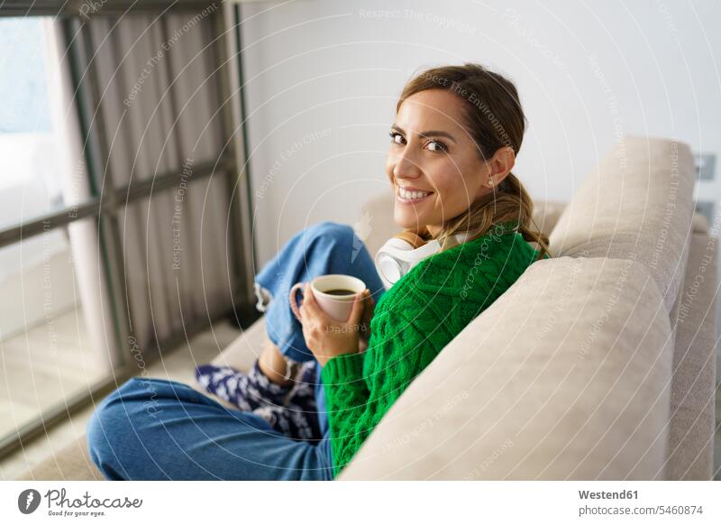 Woman drinking coffee while sitting on sofa at home color image colour image indoors indoor shot indoor shots interior interior view Interiors day daylight shot