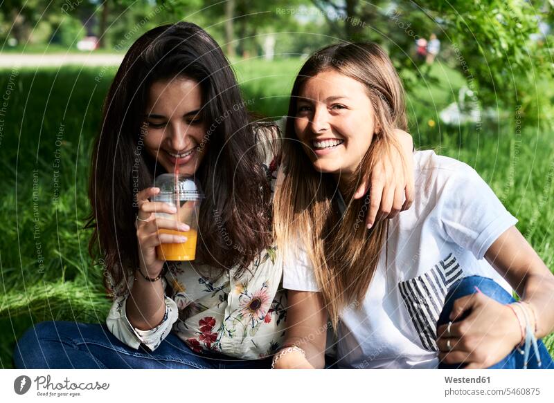 Portrait of two happy young women drinking juice at a picnic in park happiness parks woman females portrait portraits Picnic picnicking Juice Juices Adults