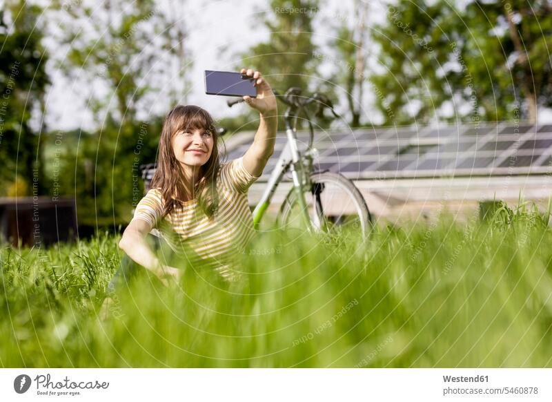 Relaxed woman sitting on a meadow with bicycle taking a selfie human human being human beings humans person persons caucasian appearance caucasian ethnicity