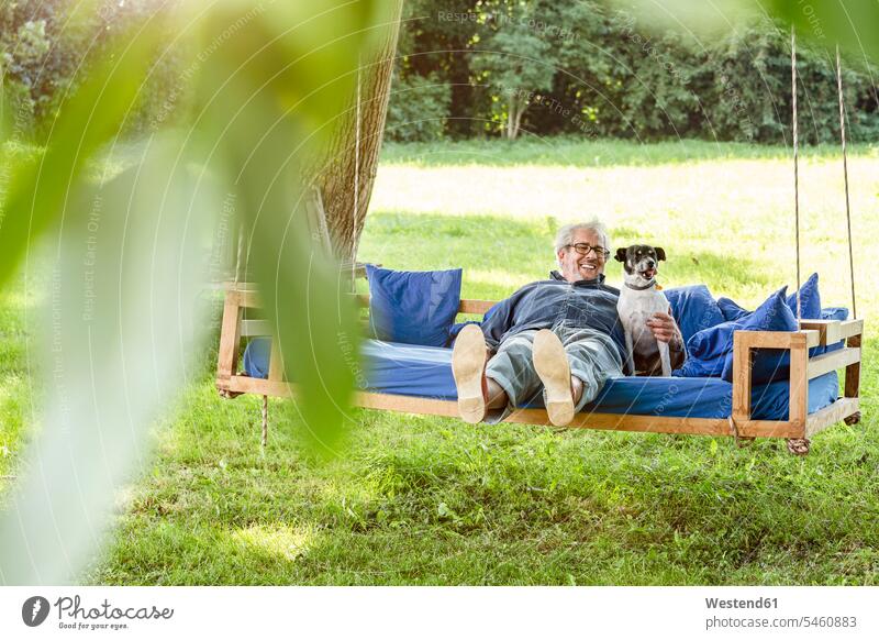 Senior man relaxing on a swing bed in his garden with his dog friendship gardens domestic garden relaxation relaxed comfortable amenities amenity confidence