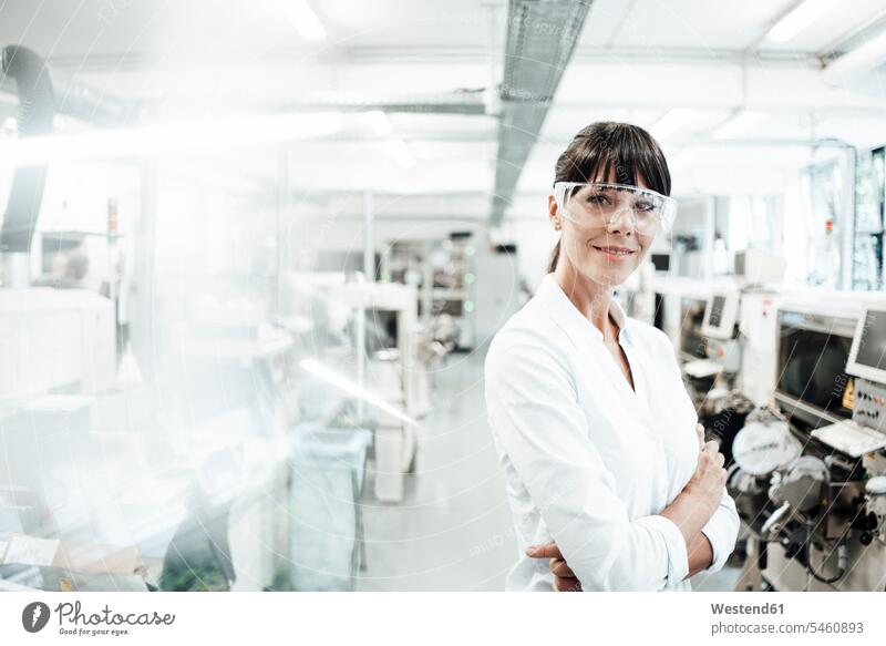 Smiling female engineer wearing protective eyewear while standing with arms crossed in industry color image colour image Germany indoors indoor shot