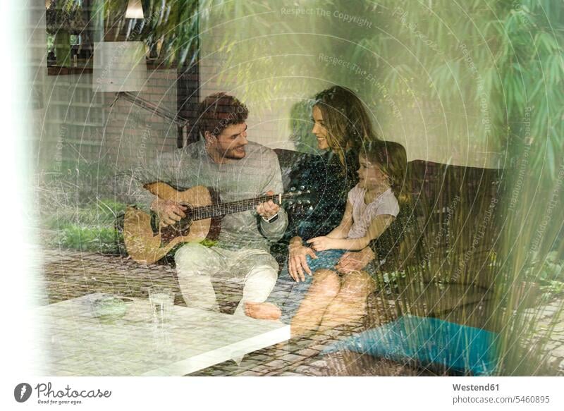 Happy parents and daughter playing guitar on sofa at home happiness happy guitars couch settee sofas couches settees daughters family families people persons