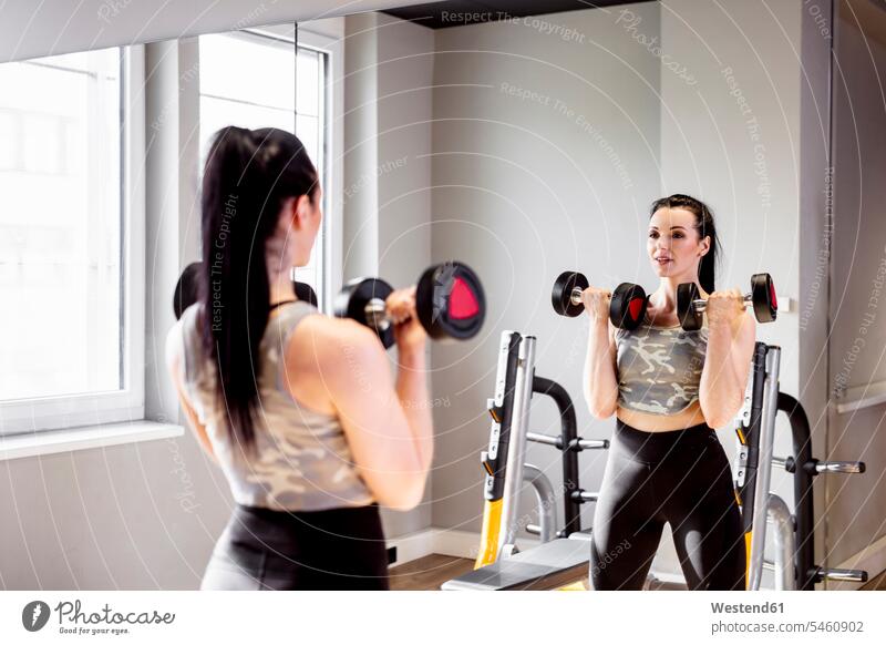 Woman lifting dumbbells in gym looking in mirror mirrors woman females women dumb-bells view seeing viewing gyms Health Club Adults grown-ups grownups adult