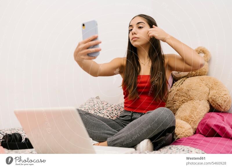 Teenage girl sitting with hand in hair while using mobile phone sitting at home color image colour image indoors indoor shot indoor shots interior interior view
