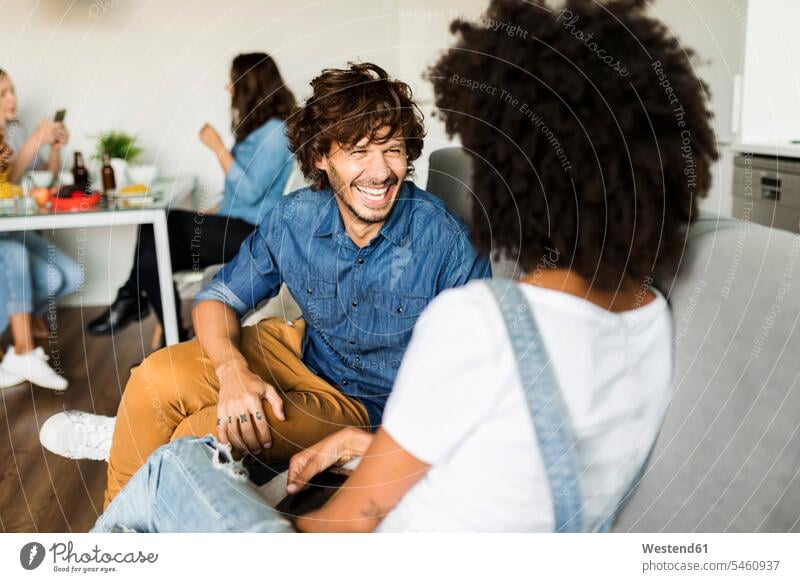 Happy couple sitting on couch talking with friends in background twosomes partnership couples happiness happy Seated settee sofa sofas couches settees people