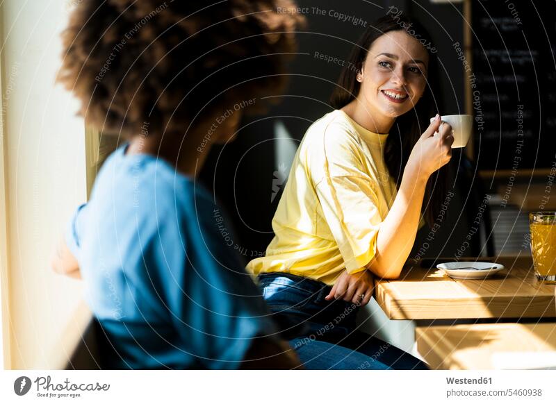 Happy woman holding coffee mug while looking friend in cafe color image colour image indoors indoor shot indoor shots interior interior view Interiors day