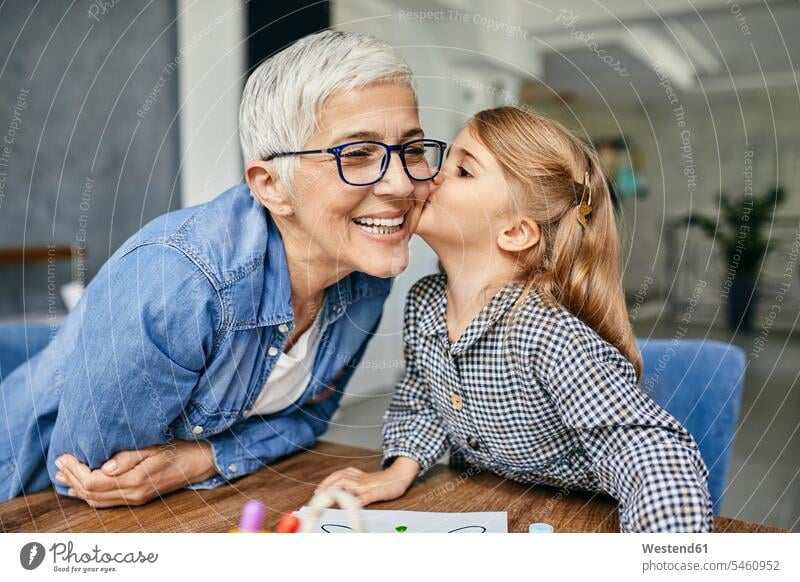 Grandduaf´ghter kissing grandmother, painting colouring book with her generation Tables kisses smile Seated sit play happy Emotions Feeling Feelings Sentiment