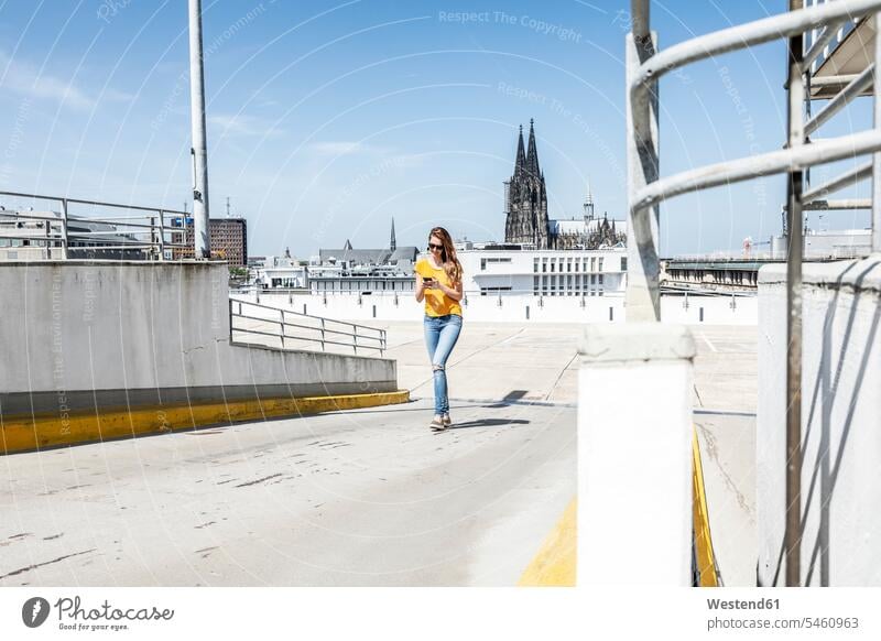 Germany, Cologne, woman walking on ramp of paking level using cell phone use parking level females women Smartphone iPhone Smartphones Ramp going parking garage