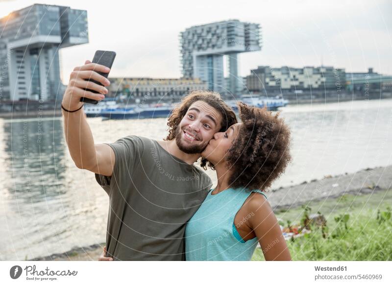Germany, Cologne, happy couple taking a selfie at the riverside happiness portrait portraits relaxed relaxation riverbank sunset sunsets sundown twosomes