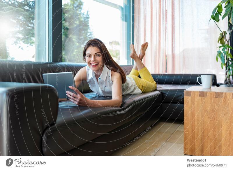 Portrait of happy woman lying on couch at home using a tablet laying down lie lying down portrait portraits digitizer Tablet Computer Tablet PC Tablet Computers