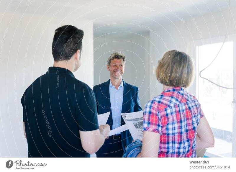 Smiling man in suit talking to couple in unfinished building construction site Building Site sites Building Sites construction sites speaking Fullsuit suits