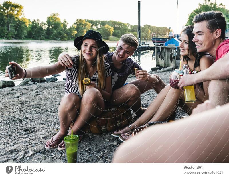 Group of friends sitting together having a barbecue and taking a selfie at the riverside Seated Selfie Selfies Barbecue BBQ Barbeque mate group of people