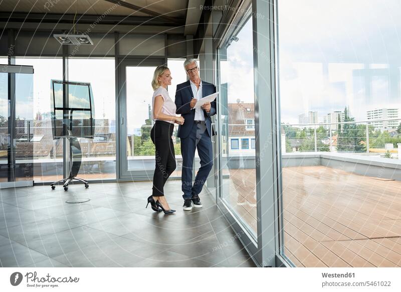 Businessman and woman standing in office, discussing project, holding documents discussion businesswoman businesswomen business woman business women