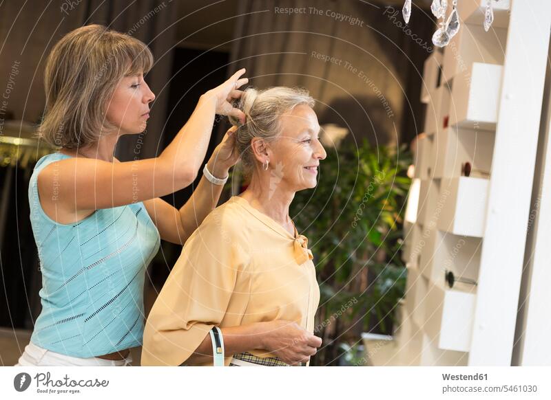 Woman helping senior woman with her hair in a shop senior women elder women elder woman old assistance assisting Help females shop assistant shop assistants