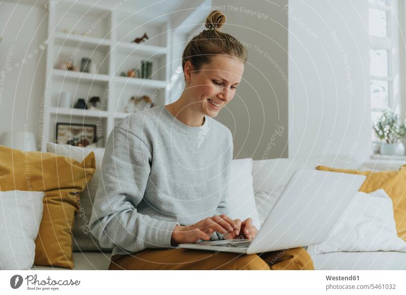 Smiling woman using laptop while sitting on sofa at home color image colour image indoors indoor shot indoor shots interior interior view Interiors day
