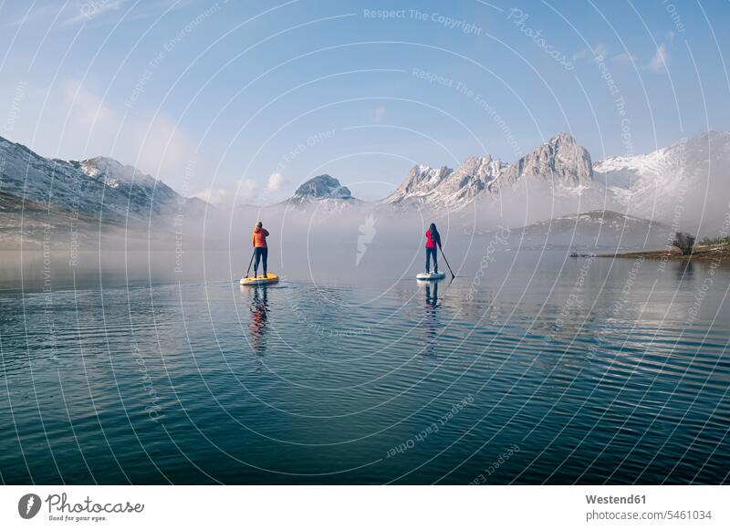 Two women stand up paddle surfing on a lake sports aquatics Water Sport watersports surf ride surf riding Surfboarding surf board surf boards surfboards