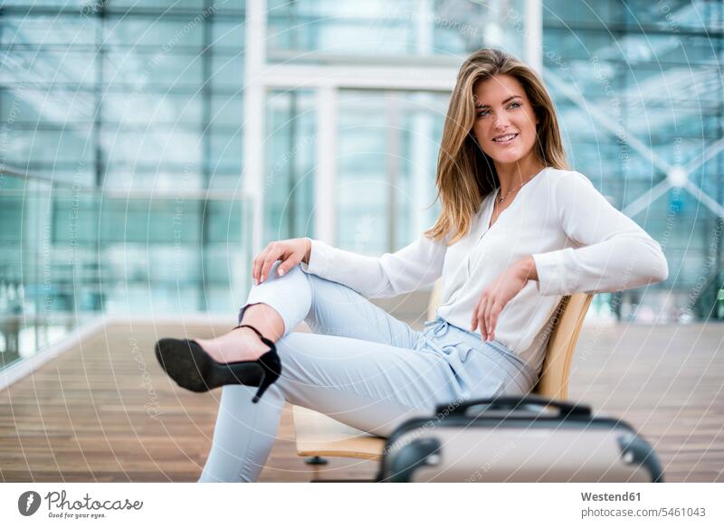 Smiling young businesswoman sitting outdoors with suitcase looking around Seated suitcases businesswomen business woman business women smiling smile